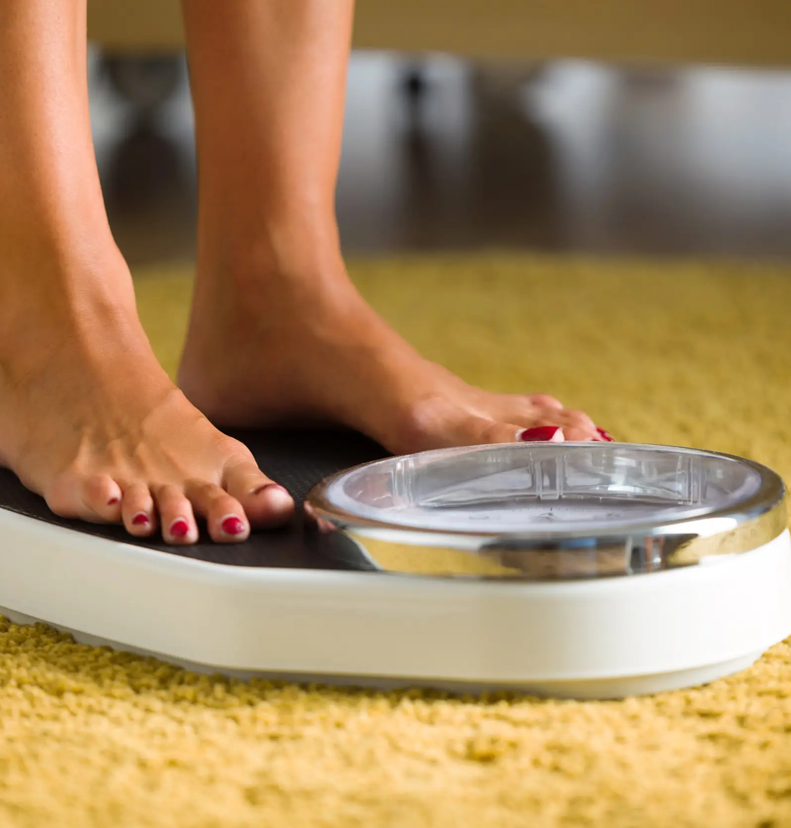 Close-up of young woman feets on weight scale at home